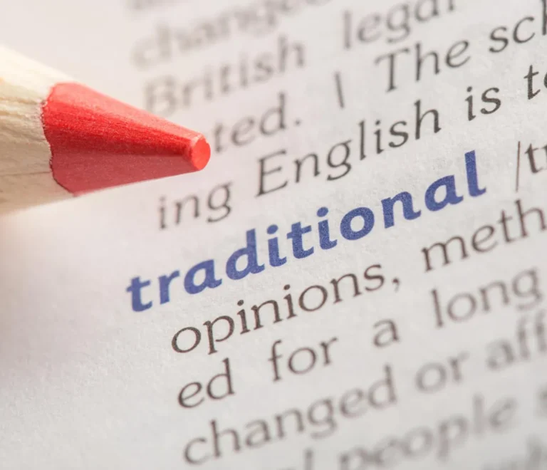 Lápiz de colores rojo apuntando a la palabra "tradicional" en una página de diccionario, destacando su definición y contexto.