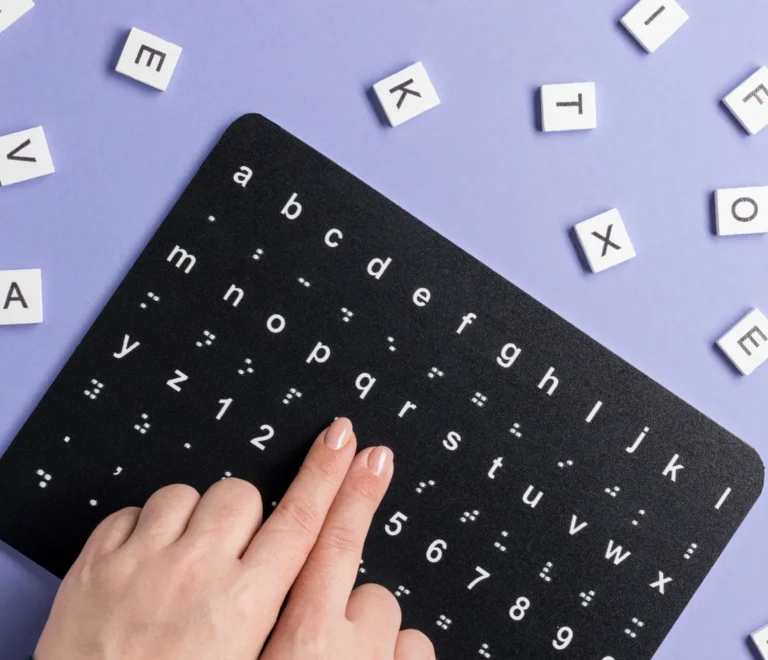 Teclado en braille con letras y números en una superficie negra, rodeado de letras blancas sobre un fondo morado. Una mano está tocando una de las teclas. Ideal para la educación inclusiva y la accesibilidad.